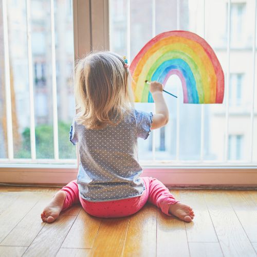 young girl painting rainbow on window