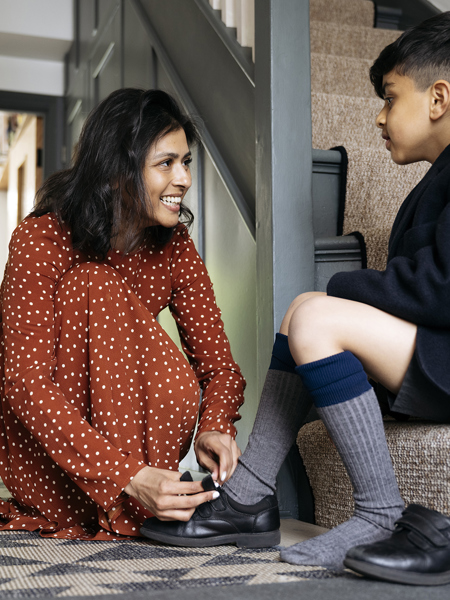 Child sitting on stairs while mother ties his shoes
