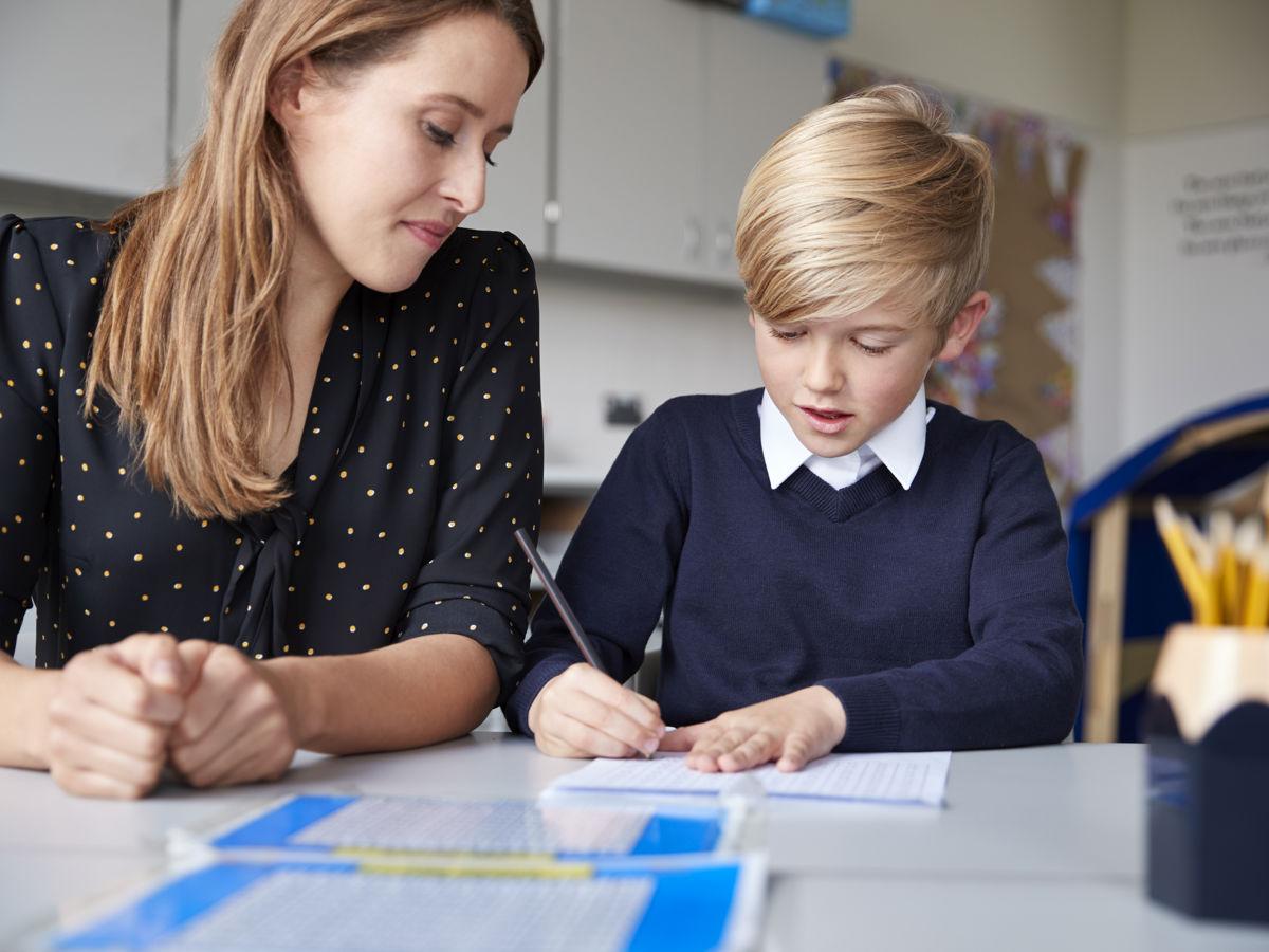 Primary school teacher and schoolboy sitting at a table working one on one