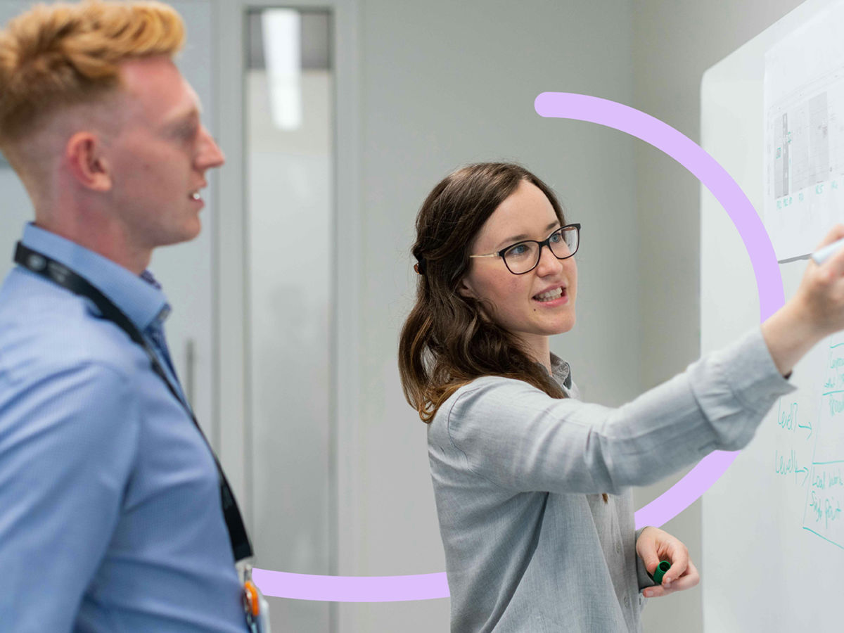 Two people in workplace setting with a whiteboard
