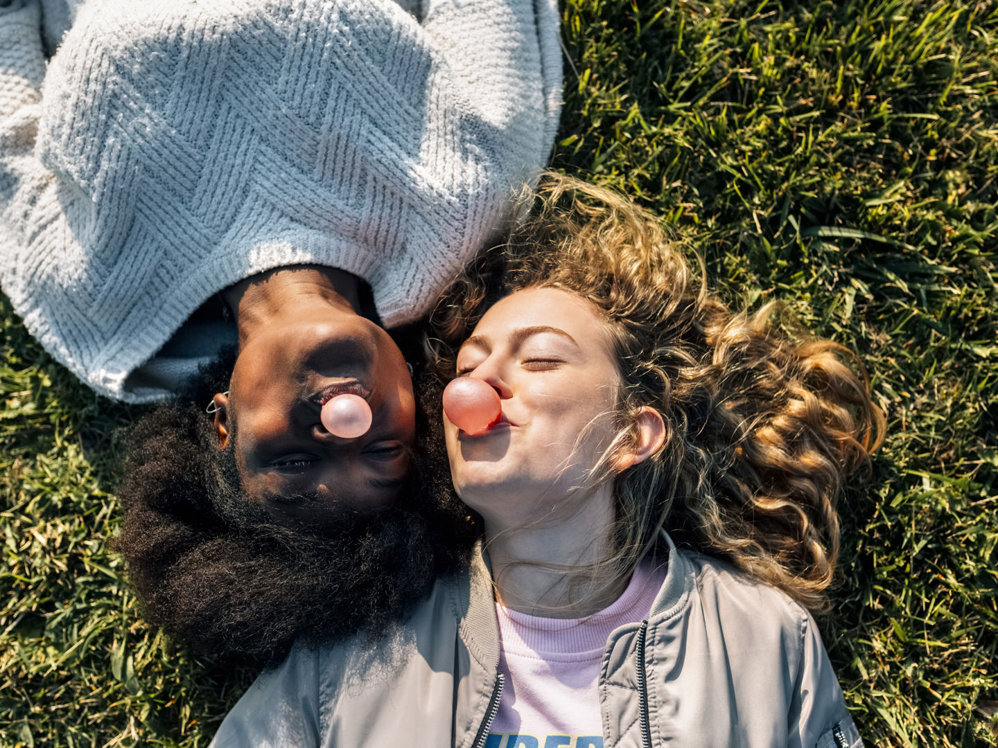 Two women lying on grass blowing bubblegum bubbles
