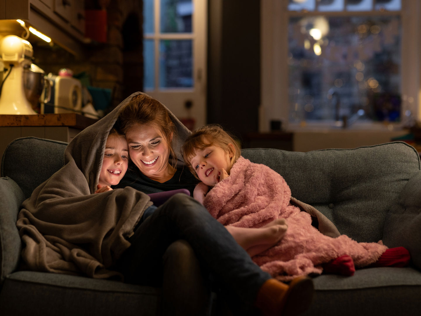 Adult with two children on the sofa at nighttime with a screen